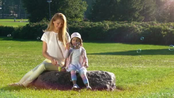 Die junge Mutter und ihre Tochter spielen im Stadtpark mit Seifenblasen. Zeitlupe — Stockvideo