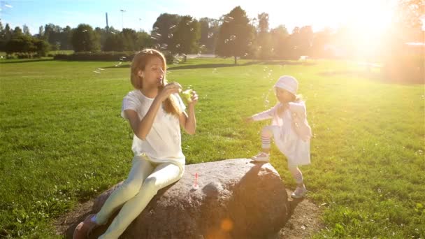 Jonge moeder en haar dochter spelen met zeepbellen in het stadspark. Slow motion — Stockvideo
