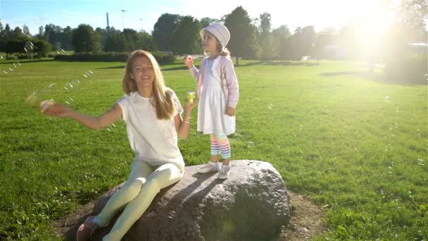 Jonge moeder en haar dochter spelen met zeepbellen in het stadspark. Slow motion — Stockvideo