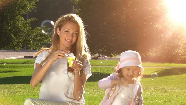 Jonge moeder en haar dochter spelen met zeepbellen in het stadspark. Slow motion — Stockvideo