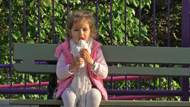 Roztomilé batole dívka jíst zmrzlinu v městském parku. Zpomalený pohyb. — Stock video