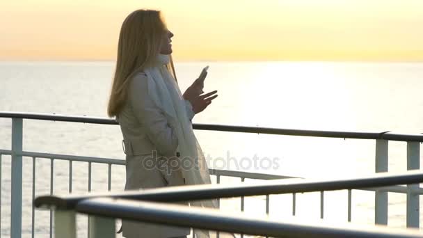 Eine junge Frau fährt mit ihrem Smartphone an Deck des Linienschiffes in der Sonne. Zeitlupe — Stockvideo
