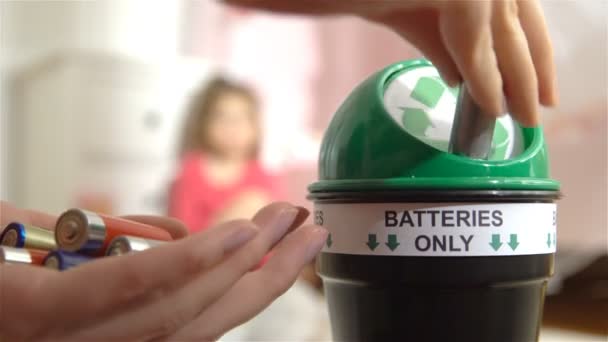 Frauenhände legen zu Hause gebrauchte Batterien in eine spezielle Recyclingbox. Kind spielt im Hintergrund. Nur Batterien. — Stockvideo