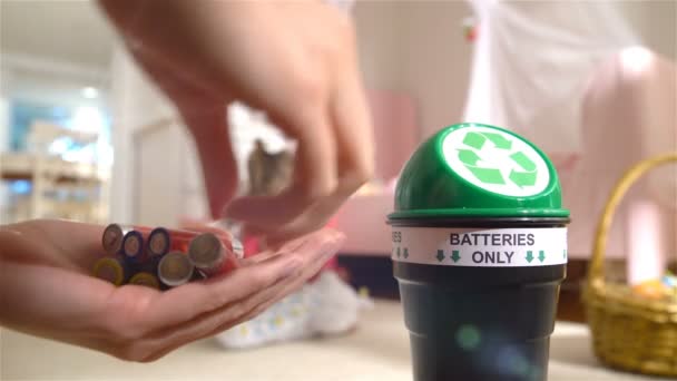 Frauenhände legen zu Hause gebrauchte Batterien in eine spezielle Recyclingbox. Kind spielt im Hintergrund. Nur Batterien. — Stockvideo