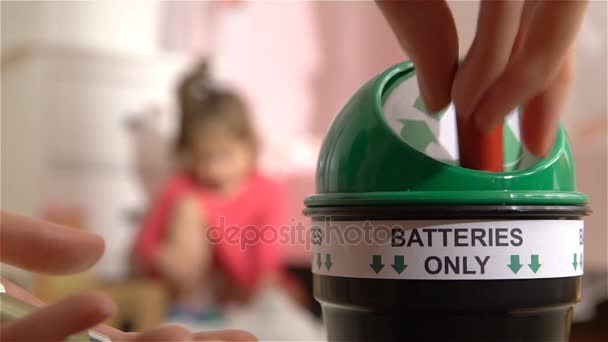 Женские руки кладут использованные батарейки в специальную коробку для переработки дома. Ребёнок играет на заднем плане. Только аккумуляторы. Медленное движение — стоковое видео