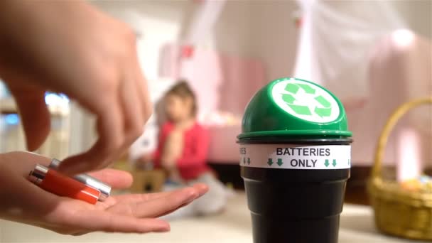 Vrouwelijke handen zetten gebruikte batterijen in speciale recycling vak thuis. Kind spelen op de achtergrond. Batterijen alleen. Slow motion — Stockvideo