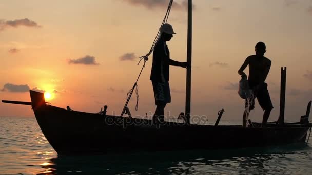 Двоє рибалок мити старі човен на заході сонця в Індійському океані. Повільний рух — стокове відео