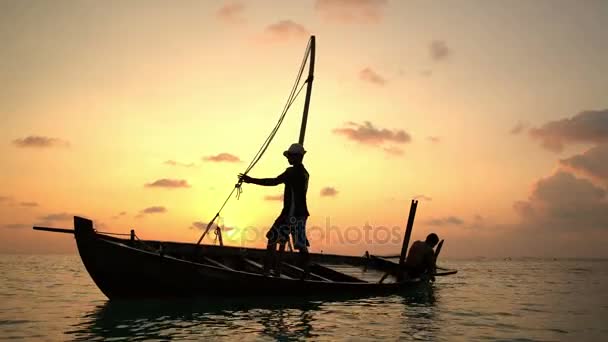 Twee vissers wassen oude boot bij zonsondergang in de Indische Oceaan. — Stockvideo