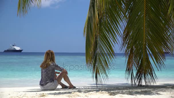 Mladá žena sedí u moře pod palm. — Stock video
