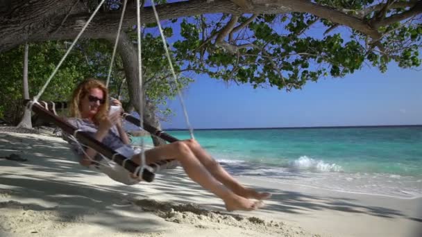 Een jonge vrouw maakt gebruik van een smartphone en geniet van de ontspannen op het tropische strand. — Stockvideo