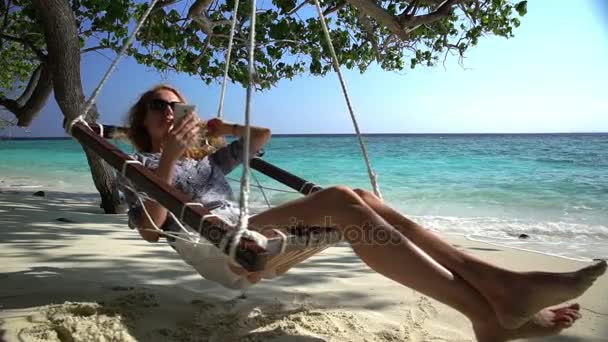 Une jeune femme utilise un smartphone et aime se détendre sur la plage tropicale . — Video