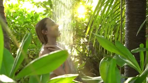 Jeune femme mince profitant d'une douche rafraîchissante dans un jardin tropical. Mouvement lent . — Video