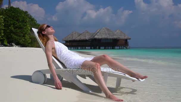 熱帯のビーチのサンラウン ジャーでの休暇を楽しんでいる若い女性。スローモーション. — ストック動画