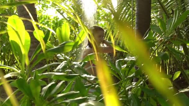 Joven mujer delgada disfrutando de una refrescante ducha en el jardín tropical. Movimiento lento . — Vídeos de Stock