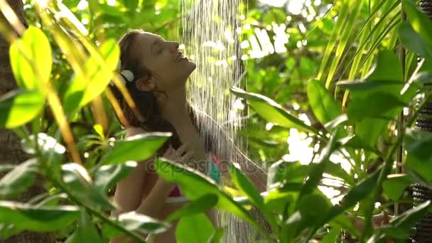Mladá štíhlá žena těší osvěžující sprcha v tropické zahradě. Zpomalený pohyb. — Stock video