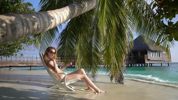 Ung smal kvinna njuter semester på en solstol på den tropiska stranden. — Stockvideo
