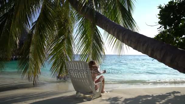 Ung smal kvinna njuter semester på en solstol på den tropiska stranden. — Stockvideo