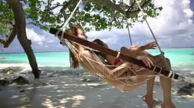 Kadın ve küçük kızı bir tropik sahilde bir hamakta tadını çıkarın.