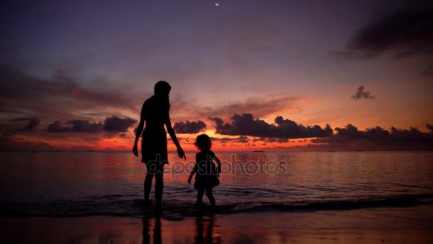 Una joven con la niña en la playa al atardecer . — Vídeos de Stock