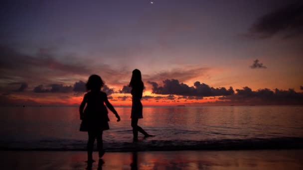 Gün batımında sahilde küçük kız olan bir genç kadın. — Stok video