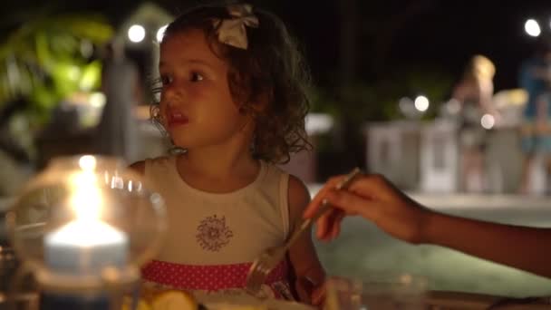 Mamá alimenta a un niño en el restaurante al aire libre por la noche . — Vídeos de Stock