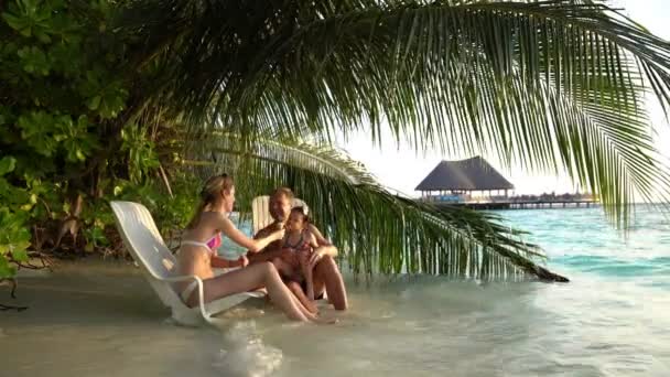 Una familia joven con un niño pequeño disfrutando de un helado en la playa tropical . — Vídeos de Stock