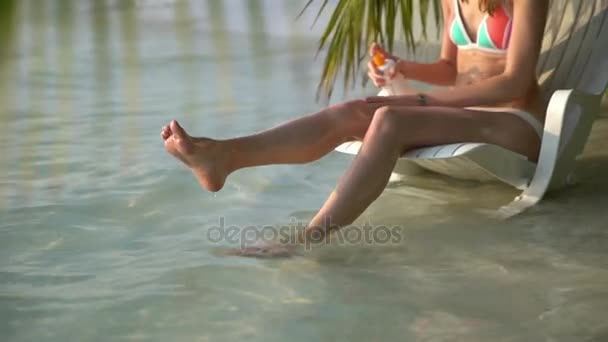 Junge Frau mit schönen Beinen benutzt Sonnencreme an einem tropischen Strand. — Stockvideo