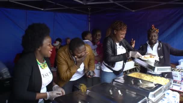 Cheerful street cooks from Cameroon offer passers-by dishes of African cuisine. They sing and dance. — Stock Video