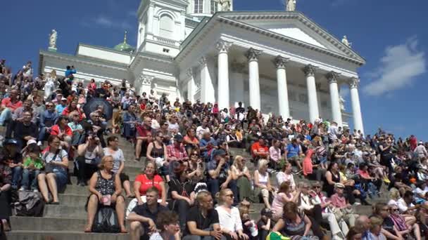 Mucha gente, estudiantes y turistas se sientan en las escaleras frente a la Catedral en la Plaza del Senado en Helsinki . — Vídeo de stock