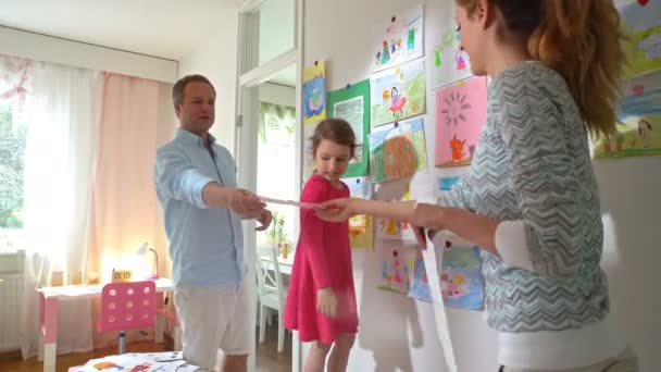 Petite fille avec parents accrocher des dessins d'enfants sur le mur dans la pépinière — Video