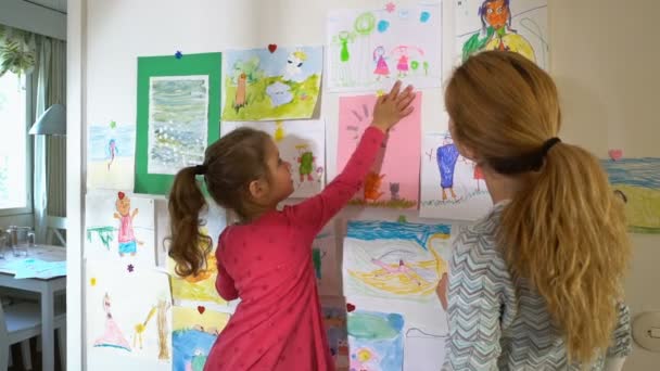 Niña con madre cuelga dibujos de niños en la pared en el vivero — Vídeos de Stock