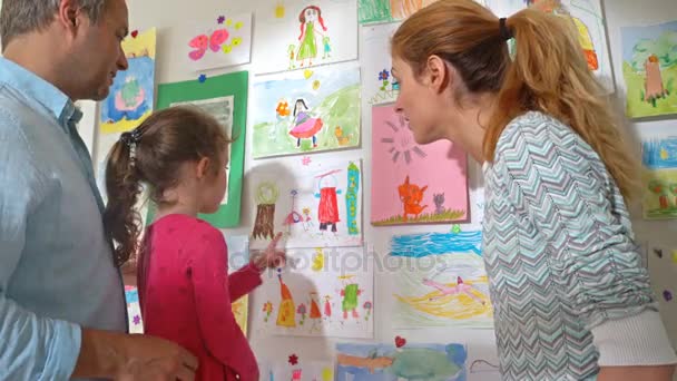 Niña con padres cuelgan dibujos de niños en la pared en el vivero — Vídeo de stock