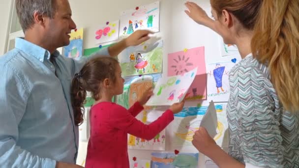 Κοριτσάκι με τους γονείς τους κρεμάστε Παιδικά σχέδια στον τοίχο στο νηπιαγωγείο — Αρχείο Βίντεο