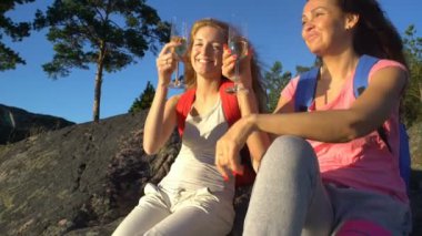 Mutlu kadın çift güneş yüksek bir kayanın üzerinde şampanya içmek