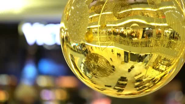 Muchos compradores en el centro comercial se refleja en una bola de oro de Navidad . — Vídeo de stock