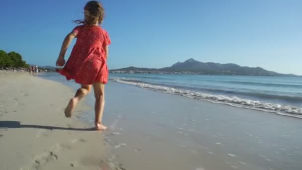 Liten flicka i röd klänning kör på stranden — Stockvideo