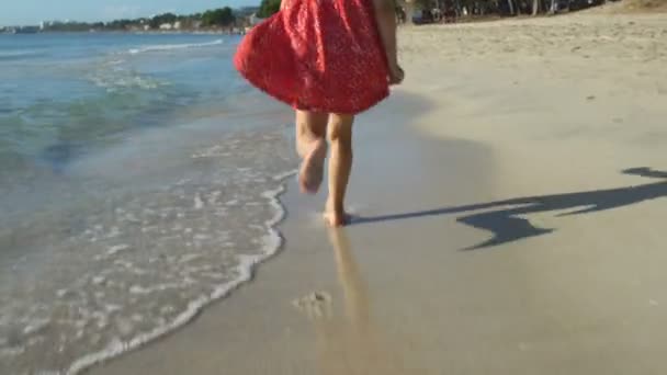 Klein meisje in de rode jurk draait op het strand — Stockvideo