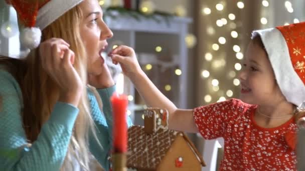 Ung mamma och bedårande dotter i röd hatt bygga pepparkakshus tillsammans. — Stockvideo