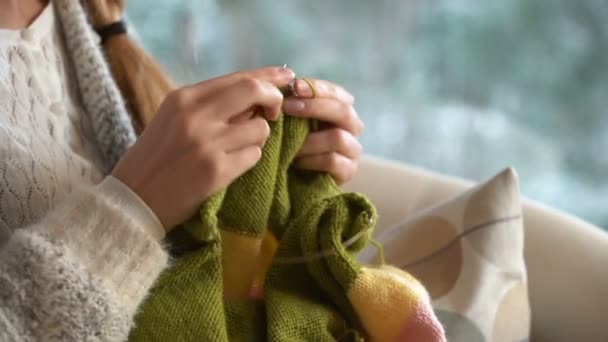 Junge Frau strickt warmen Wollpullover im Wohnzimmer gegen Schneelandschaft von außen. — Stockvideo