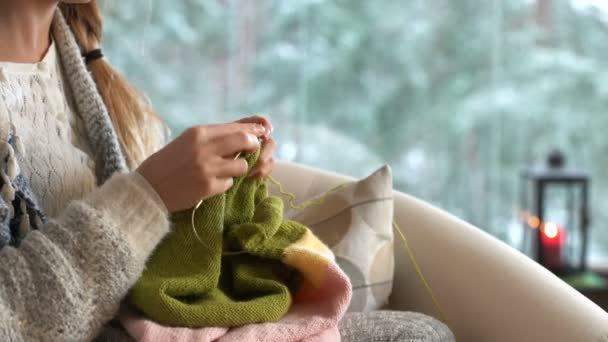 Mujer joven tejiendo suéter de lana caliente en la sala de estar contra el paisaje de nieve desde el exterior . — Vídeos de Stock