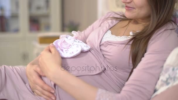 Junge schwangere Frau sieht winzige Booties. — Stockvideo