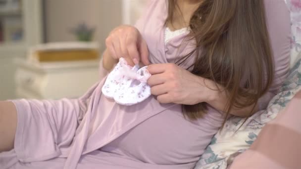 Junge schwangere Frau sieht winzige Booties. — Stockvideo