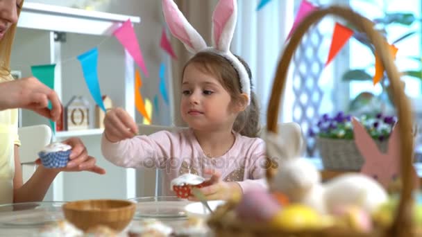 Young mother and her little daughter with rabbit ears cooking Easter cupcakes — Stock Video