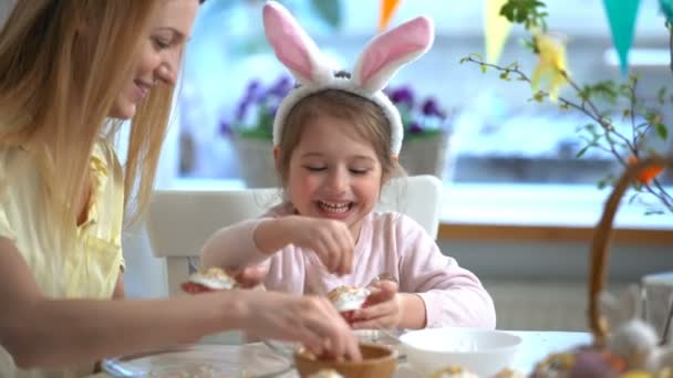 Young mother and her little daughter with rabbit ears cooking Easter cupcakes — Stock Video