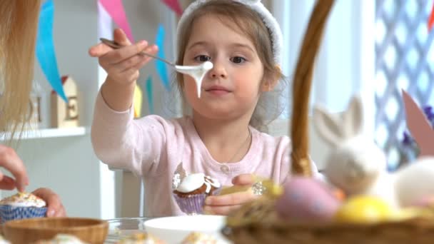 Jovem mãe e sua filha vestindo orelhas de coelho cozinhar cupcakes de Páscoa — Vídeo de Stock