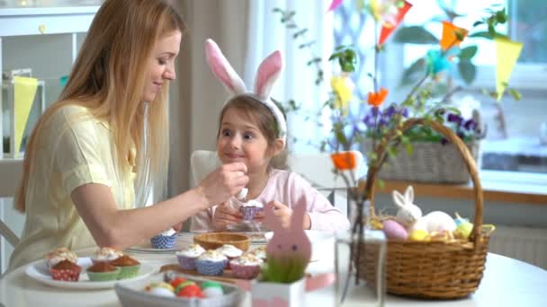 Jovem mãe e sua filha vestindo orelhas de coelho cozinhar cupcakes de Páscoa — Vídeo de Stock