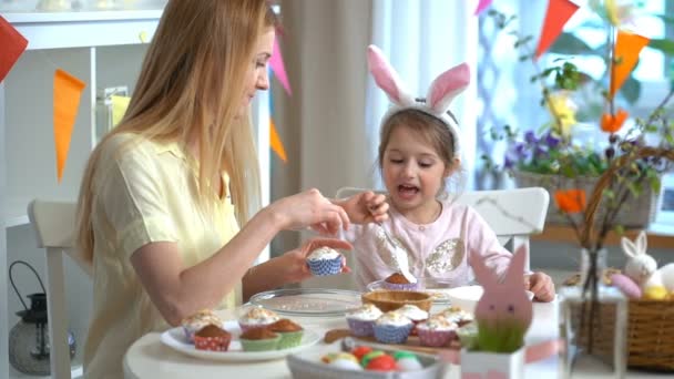 Молодая мать и ее дочь носят кроличьи уши и готовят пасхальные кексы — стоковое видео