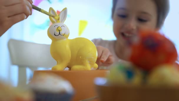 Glückliche Ostermutter und ihre kleine Tochter mit Hasenohren beim Bemalen des Osterhasen — Stockvideo