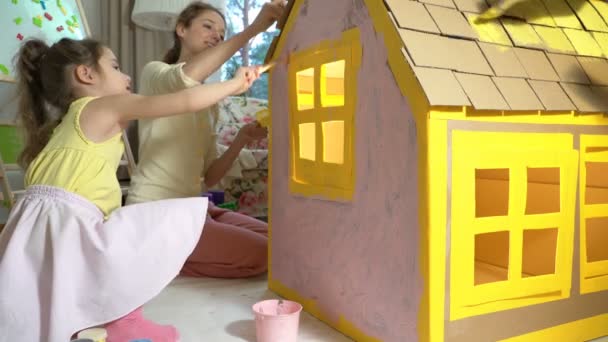 Jong gezin met kind bouwen en schilderen speelgoed kartonnen huis samen. — Stockvideo