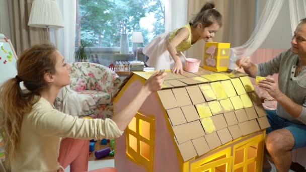 Mladá rodina s dítětem, budování a malbou hračka kartónové house. — Stock video